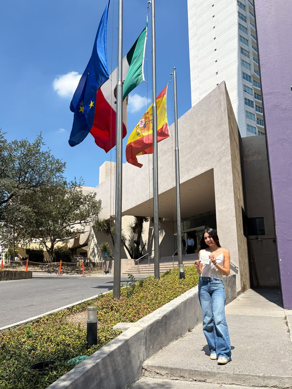 Client holding a consular document in front of the consulate with EU, Mexican and Spanish flags